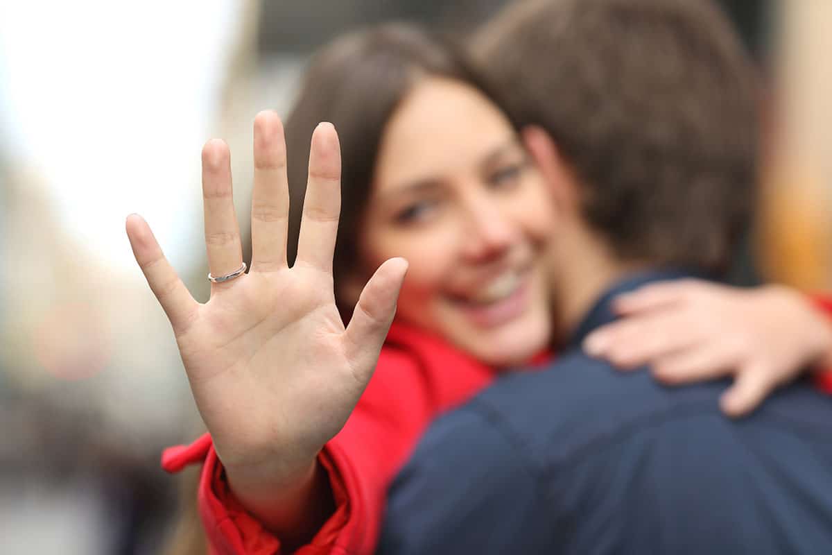 woman raising her hand to display her new engagement ring while hugging her fiance.